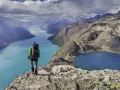 Vandrare med ryggsäck står på en klippa och blickar ut över turkosa sjöar och berg i Jotunheimen nationalpark.