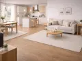 Ljust och luftigt vardagsrum med kök i öppen planlösning. En soffa, soffbord och matplats med stolar. Allt är inrett med mattor som skapar en mysig atmosfär.
