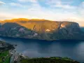 En vy över Sognefjorden med solbelysta berg och en liten by vid vattnet. Som en levande sognefjorden karta.