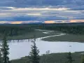 En slingrande flod genom ett vidsträckt skoglandskap i Muddus nationalpark. Molnen på himlen färgas av solnedgången.