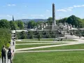 Vigelandsparken med dess imponerande monoliten och skulpturer, en solig dag med besökare som njuter av parken.