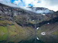 En spegelblank sjö reflekterar en dramatisk bergssida med en forsande vattenfall. Perfekt för att vandra i Abisko.