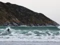 En ensam surfare kämpar mot en kraftig våg vid kusten i Norge. Den dramatiska bergssidan bakom ger en mäktig kuliss för detta äventyr.