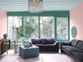 Ett vardagsrum med art deco inredning, mjuklila soffa, mörkgrå soffa, turkos pall och en stor fönsterutsikt.