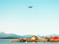 Ett flygplan närmar sig landning vid Molde, Norge. Röda och gula bodar står vid vattnet med berg i bakgrunden.