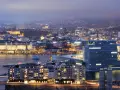 Fakta om Oslo: En stad vid vattnet med moderna byggnader och upplysta hus, som sträcker sig mot en kulle i fjärran.