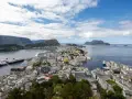Vacker vy över Ålesund, Norge, med färgglada hus, fartyg i hamnen och berg i bakgrunden under en molnig himmel.