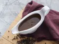 En vit såsslev fylld med mustig brunsås, bredvid en hög med svartpepparkorn. Ett perfekt brunsås recept för middagen.