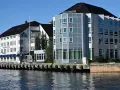 Hotellbygg vid vattnet i Arendal, Norge. En vit byggnad med blå markiser och en modern glasbyggnad står sida vid sida.