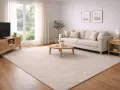 Ett ljust och luftigt beige vardagsrum med en stor soffa, soffbord och TV-bänk. En stor, mjuk matta täcker golvet.