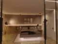 Sovrum med modern belysning. En säng med mörka sängkläder står på en matta. Väggen bakom sängen har en textur och är upplyst av LED-lister. Golvet är parkett.