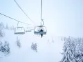En skidåkare åker linbana uppför ett snötäckt berg i Norge, omgiven av frostiga träd.