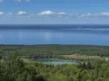 Vacker utsikt över en sjö och en grönskande skog. En liten sjö med klippor syns i mitten, en del av **Götaleden etapp 7**.