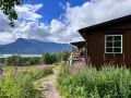 En brun stuga vid en blomsteräng med fjäll i bakgrunden. En stig leder mot stugan, en del av Kungsleden i Sarek.