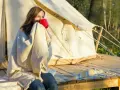 Kvinna med filt och röd mugg vid tältet. En perfekt packlista camping-morgon.