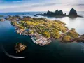 En pittoresk by på en ö i Norge, med berg i bakgrunden. En båt lämnar ett spår i vattnet. En vacker vy över traena norge.