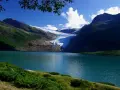 Blå sjö vid foten av en glaciär i Steinkjer, Norge. Grönskande bergssluttningar möter det turkosa vattnet under en klarblå himmel.