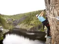En person klättrar på en klippa vid rypetoppen adventurepark. Vacker natur med sjö och skog.