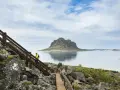 Vandrare på trappor vid havet med en imponerande bergstopp i bakgrunden, en vy från Vega Norge.
