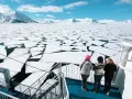 Besök Svalbard och se isflak som bryts upp i ett arktiskt landskap. Tre personer står på ett fartyg och blickar ut över det frusna havet.