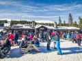 Folk njuter av afterski i Trysil vid en mysig timmerstuga med snöklädda berg och granar i bakgrunden.
