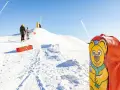 En glad björn pryder en pulka backe. Barn klädda för kyla väntar på sin tur att åka nerför den snöiga kullen.