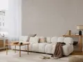 Ett ljust vardagsrum med japandi inredning. En vit soffa med textur, träbord, kuddar och en brun pläd. Bakom soffan en tapet med vågiga linjer.