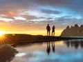 Två silhuetter står på en klippa vid havet och ser på solnedgången över Bodo, Norge. Bergskedja i bakgrunden.