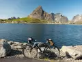 En cykel står vid en sjö med berg och en by i bakgrunden. Perfekt för mtb norge-äventyr.