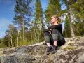Kvinna sitter på en klippa i skogen, njuter av utsikten. Kanske en paus under vandringen i Folgefonna nationalpark.