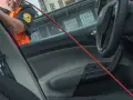 En person i orange väst använder ett rött verktyg för att öppna en bildörr. Kanske glömde de dnt nyckel därinne.