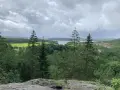 Vacker utsikt över sjö och skog, perfekt för vandringsleder Alingsås. Molnig himmel över det gröna landskapet.