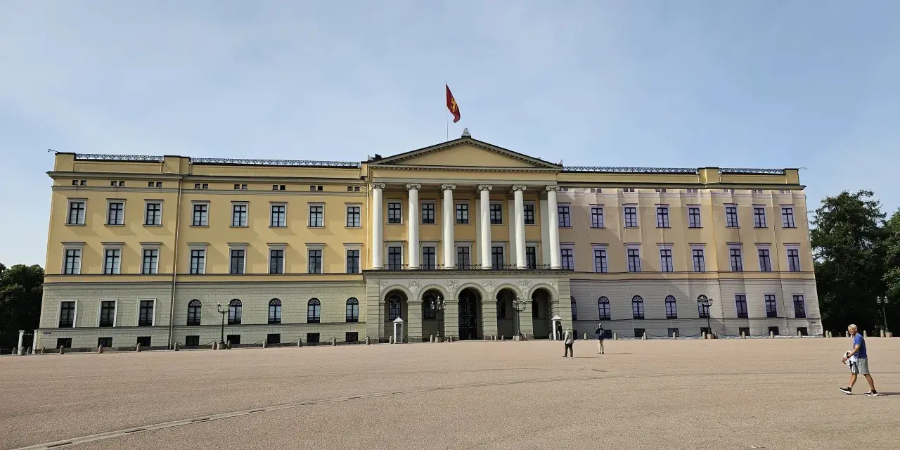 Det gula **Oslo slott** med sin flagga reser sig stolt mot en klarblå himmel. En stor öppen plats framför slottet.