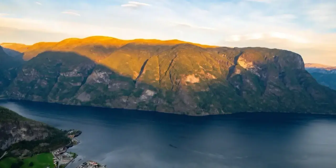 En vy över Sognefjorden med solbelysta berg och en liten by vid vattnet. Som en levande sognefjorden karta.