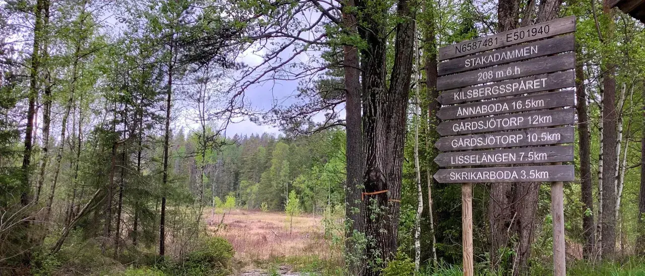 Skylt vid Kilsbergens vandringsled visar vägen till Stakadämmen och andra platser. En vacker skogsmiljö.