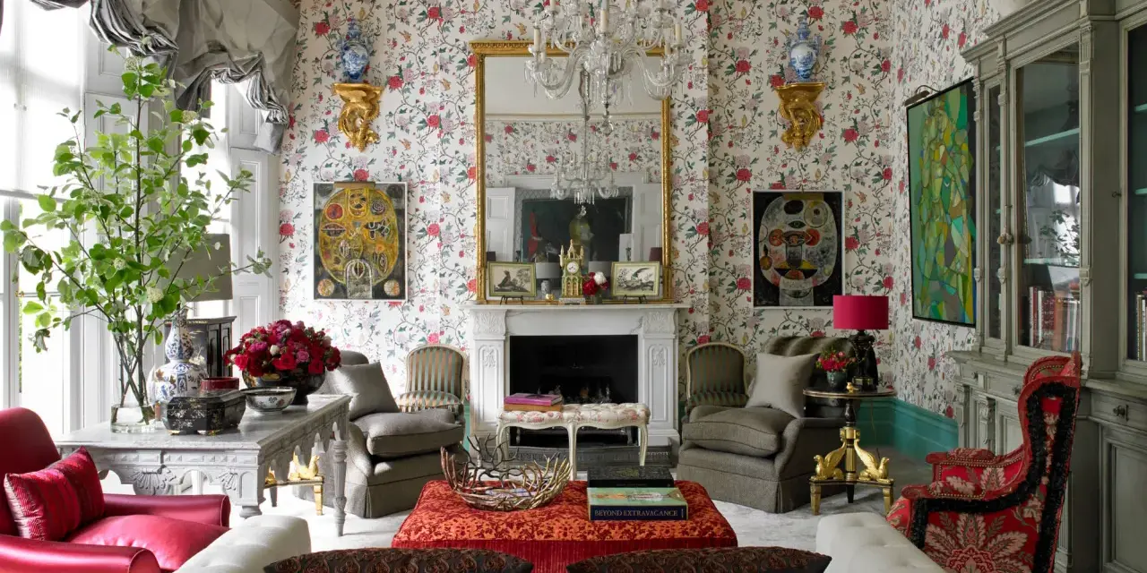 Maximalism inredning med blommig tapet, kristallkrona, röda och grå möbler samt konstverk.