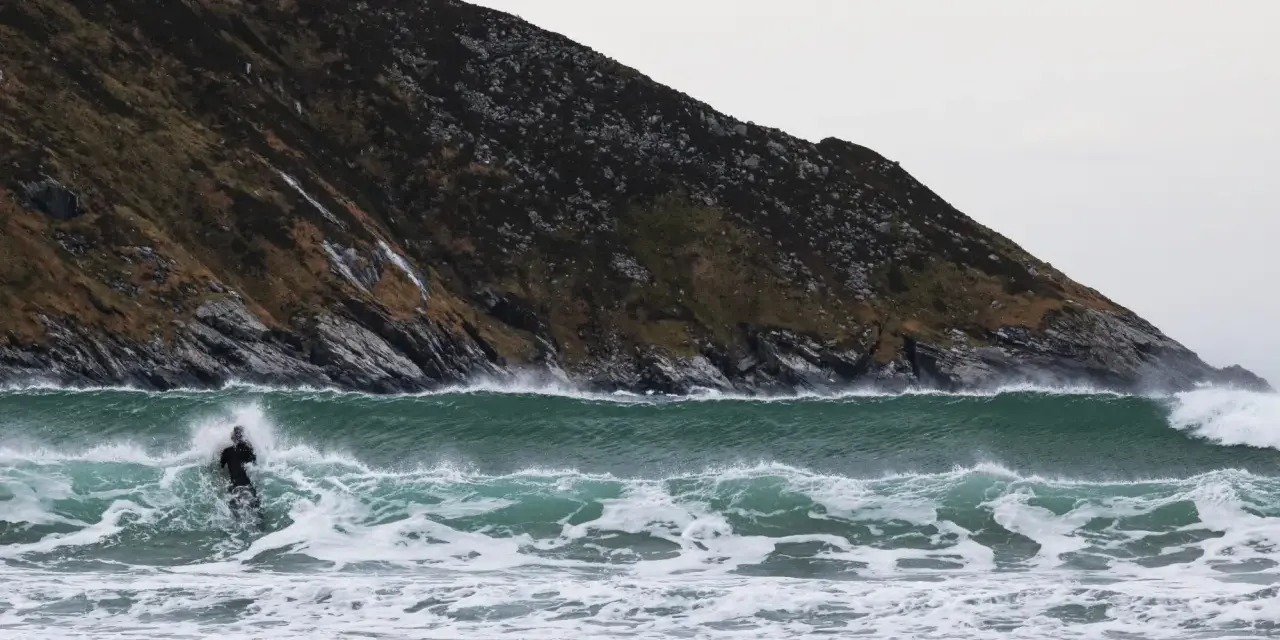 En ensam surfare kämpar mot en kraftig våg vid kusten i Norge. Den dramatiska bergssidan bakom ger en mäktig kuliss för detta äventyr.