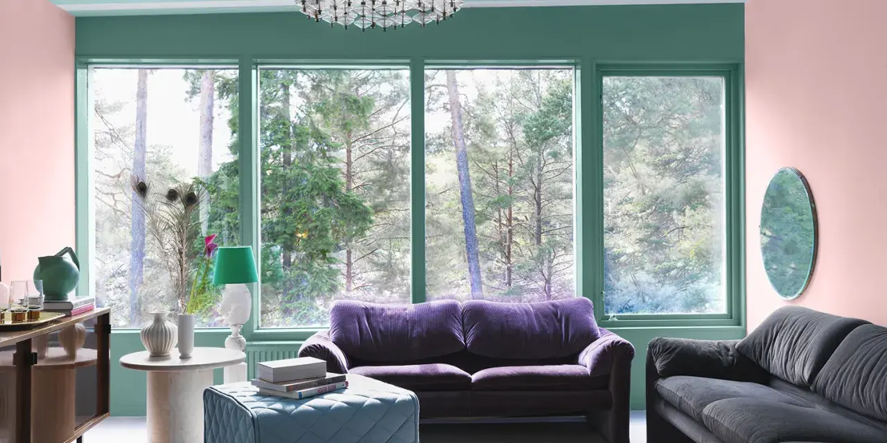 Ett vardagsrum med art deco inredning, mjuklila soffa, mörkgrå soffa, turkos pall och en stor fönsterutsikt.