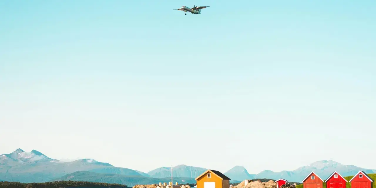 Ett flygplan närmar sig landning vid Molde, Norge. Röda och gula bodar står vid vattnet med berg i bakgrunden.
