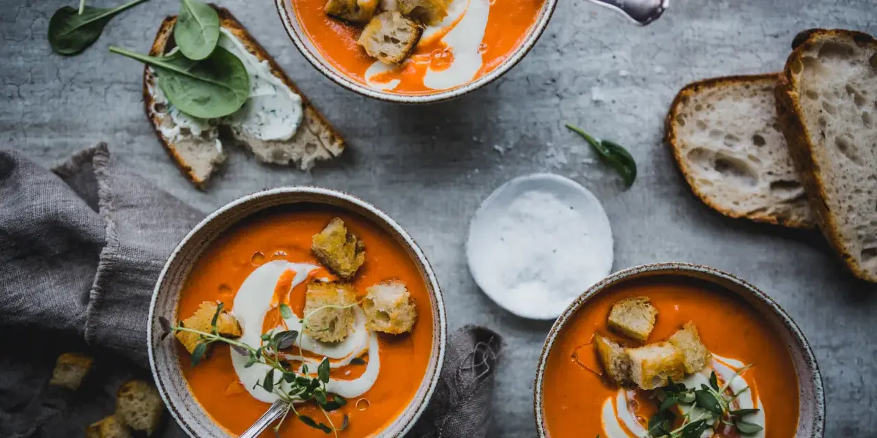 Tre skålar med krämig tomatsoppa, toppad med krutonger och en virvel av grädde. Perfekt för ett mysigt tomatsoppa recept.