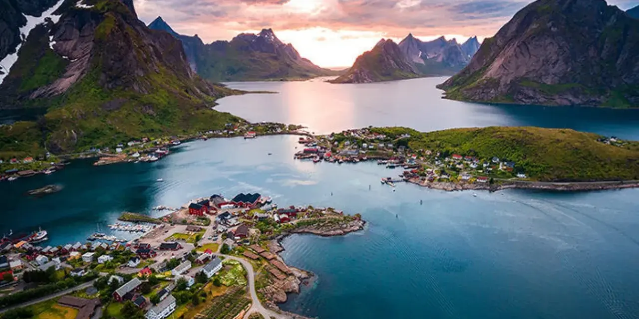 En pittoresk by med röda hus vid en fjord, omgiven av dramatiska berg. En av de fina platserna i Norge, badande i solnedgångens ljus.