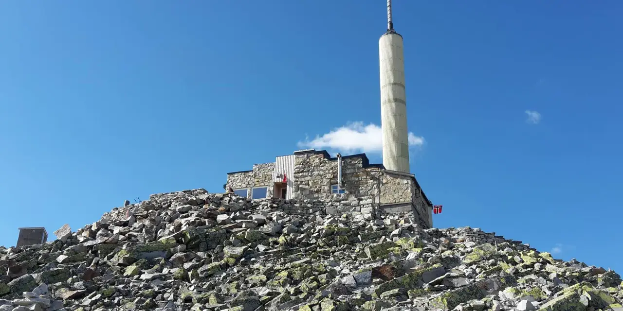 Stone building with a tall tower on a rocky mountain peak under a blue sky.