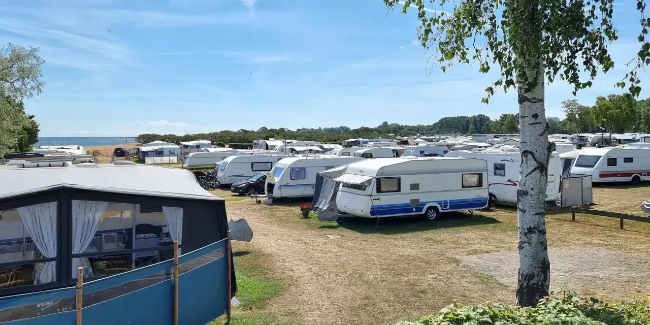 En stor campingplats med många husvagnar. Solen skiner och himlen är blå.