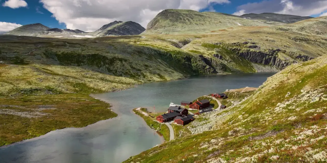 En vacker vy över en sjö med röda stugor vid en fjällsluttning, perfekt för en triangeltur i Norge.