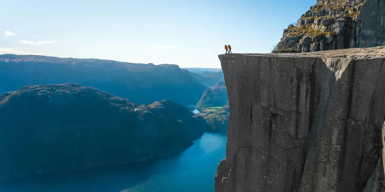 Två personer står på kanten av en klippa med utsikt över Stavangerfjorden.