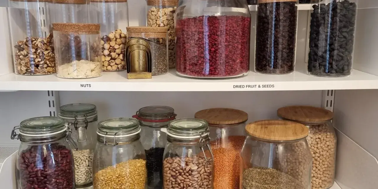 Snyggt organiserat skafferi med glasburkar fyllda med nötter, torkad frukt, frön och baljväxter. Enkelhet och ordning för att organisera skafferi.