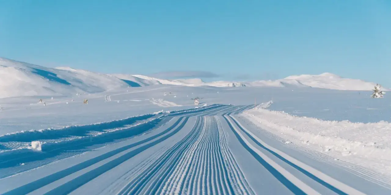 Perfekt preparerade spår för längdskidåkning i Hemsedal. Solen lyser på de snötäckta bergen och den blå himlen.