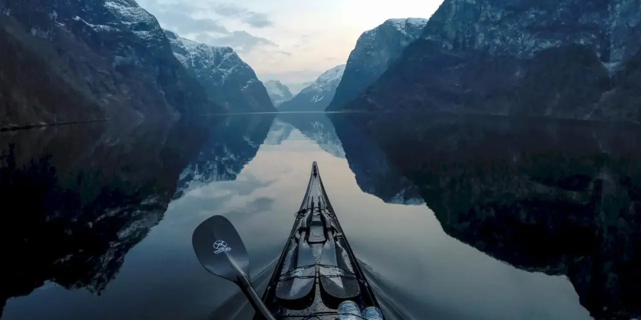 Kajakpaddling i en norsk fjord med snöklädda berg som speglar sig i det lugna vattnet. En fantastisk utsikt över son Norge.