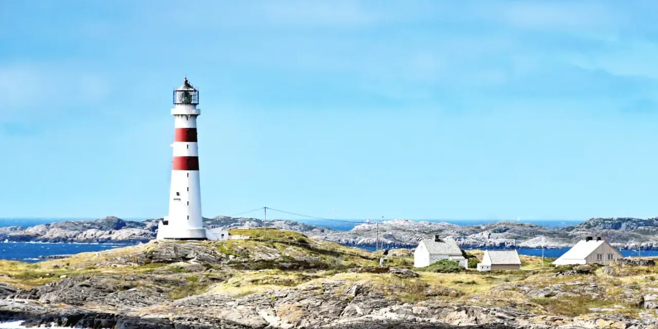 Rött och vitt fyr på en klippig ö nära Kristiansand, Norge. Små vita hus ligger utspridda på ön.