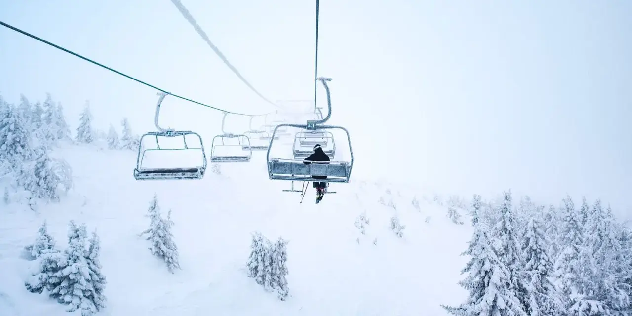 En skidåkare åker linbana uppför ett snötäckt berg i Norge, omgiven av frostiga träd.